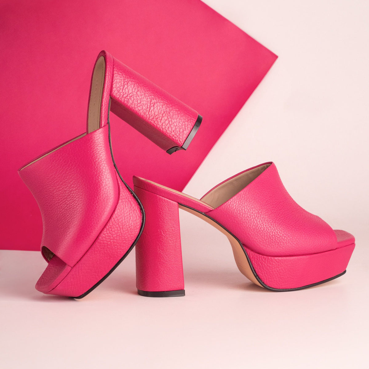 Pair of bright pink platform heeled sandals against a pink and pale pink background