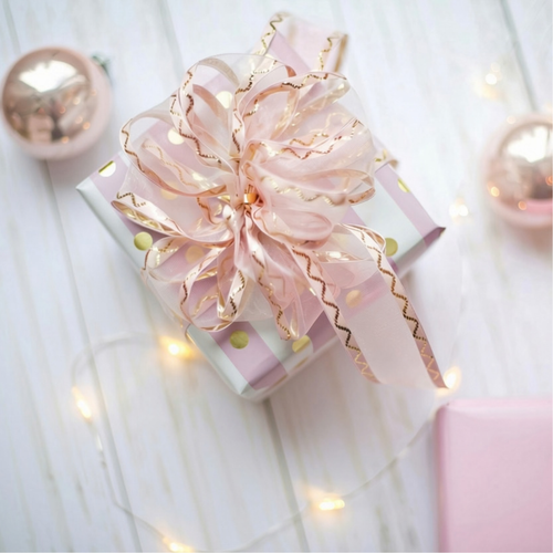 Pink and white holiday gift boxes with a large pink ribbon and warm string lights